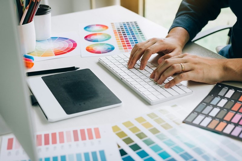 A representation of a designer working on a computer with color palettes and creative assets spread across a desk.