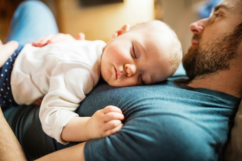 a baby sleeping on his dad's stomach.