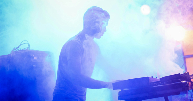A representation of a man playing a keyboard at a concert with lights and smoke