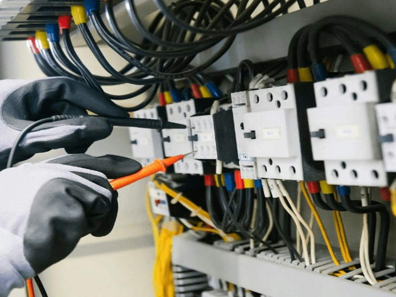 A pair of an electrician's hands in workmen's gloves, testing faulty wiring (stock).