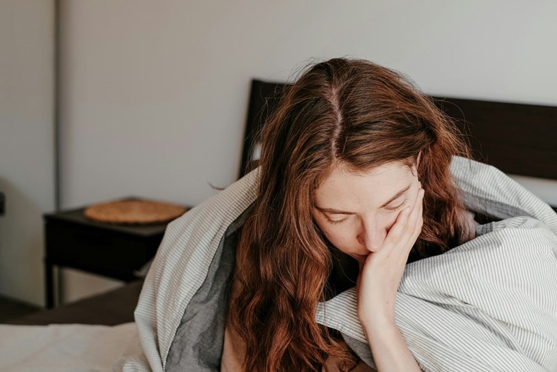 A woman sitting on her bed with her hair down looking down.