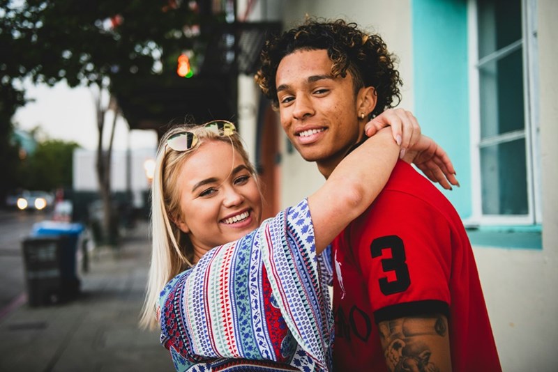 A young couple embraces each other a young man in a red shirt and young woman with a care-free vibe