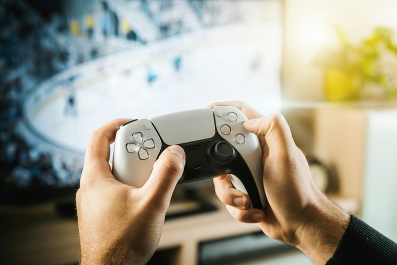 Person holding a PS5 game controller while playing on a TV screen.