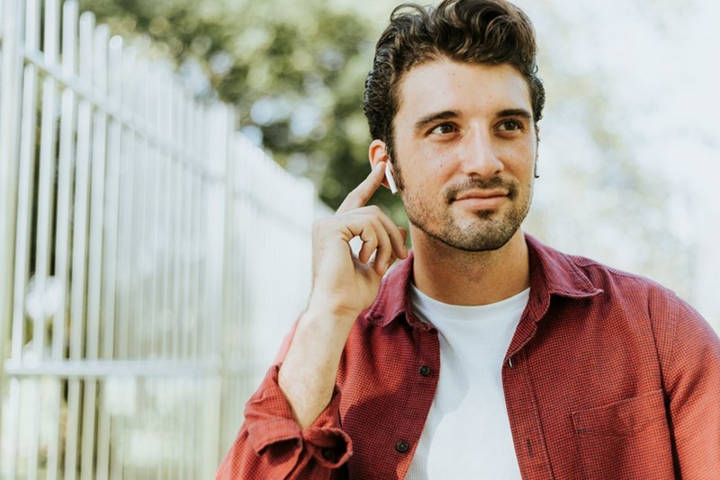Young professional listening with wireless earbuds in an outdoor setting.