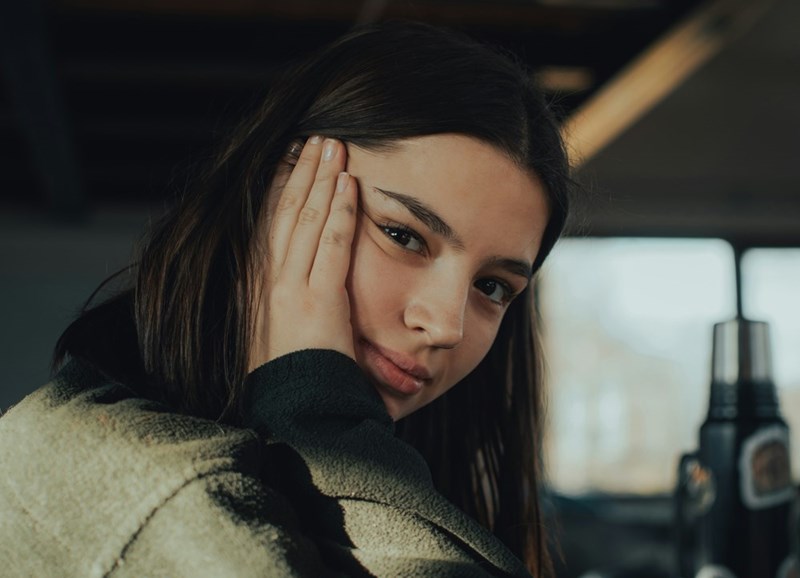 Woman resting her head on her hand with a bothered expression in a softly lit indoor setting.