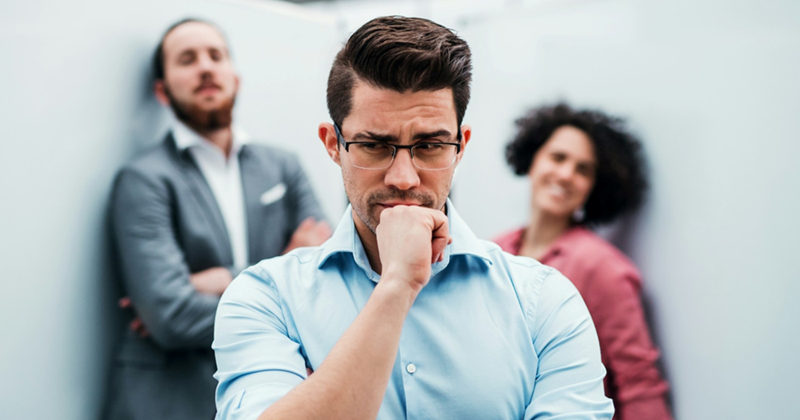 A representation of an employee in holding his hand to his face in thought, with two colleagues on either side of him in the background