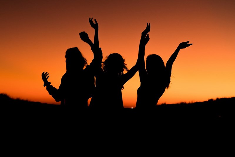 silhouette of three women with their hands in the air during sunset