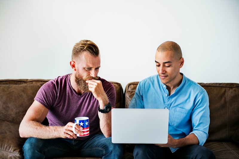 Two men sitting on a couch looking at a computer.