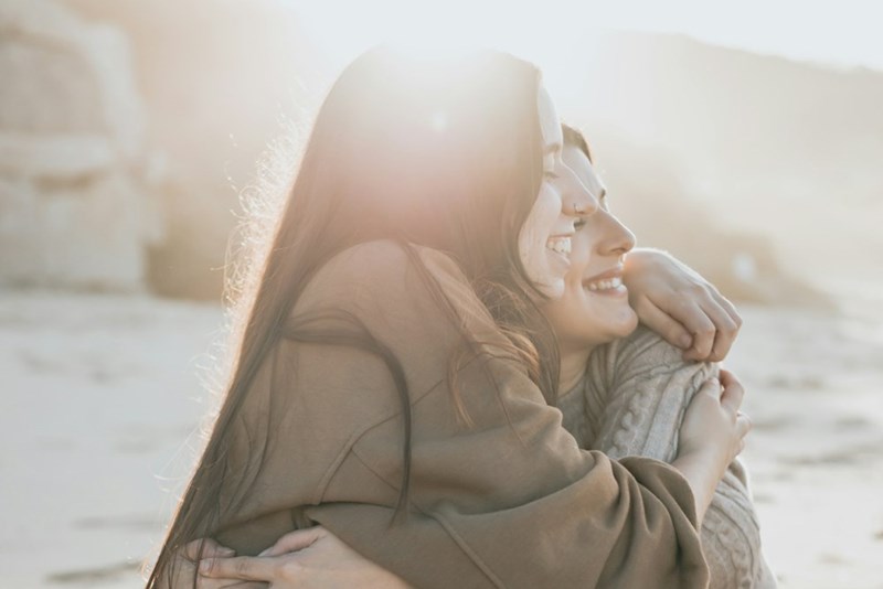 Two friends embracing and smiling outdoors at sunset.