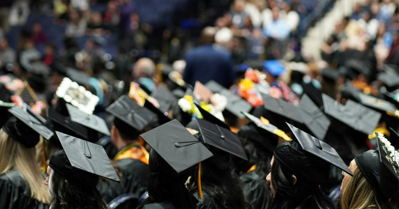 A large group of students sitting inside wearing caps and gowns
