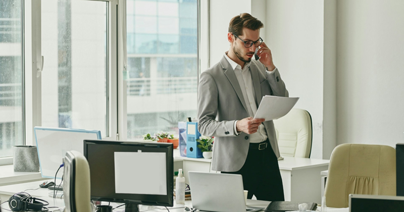 A representation of an employee standing in his office, talking on his cellphone, and looking at some papers