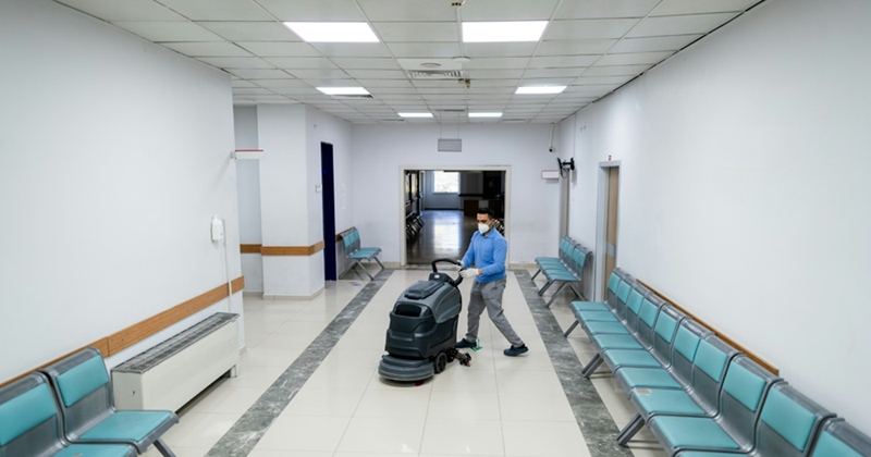 A representation of a man using a floor cleaning machine in a waiting area lined with seats
