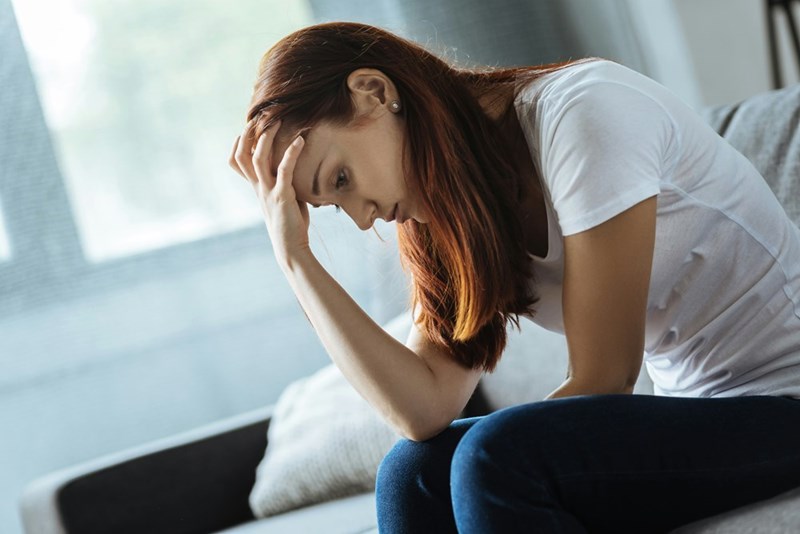 Woman sitting on a sofa with her hand on her head looking upset.