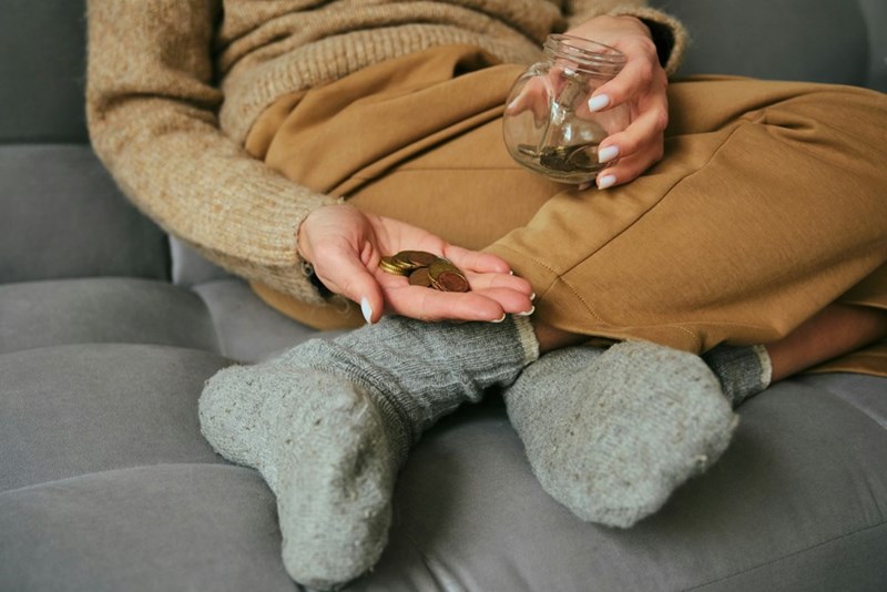Woman curled up on a couch holding coins on her hand.