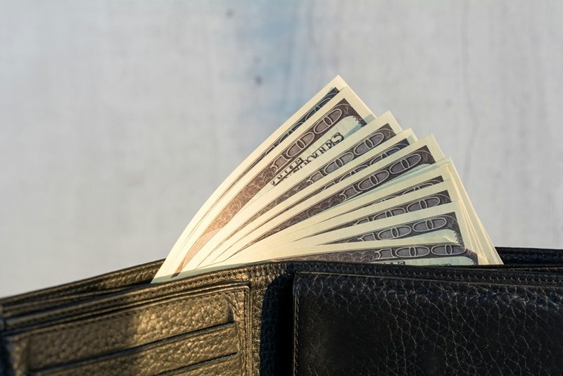 A wallet with a stack of twenty dollar bills.