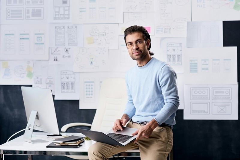 Modern young office worker (model) sitting at a desk, working on his laptop