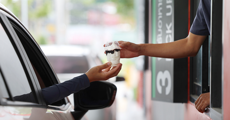Image representing a man in a car receiving coffee in a drive-thru fast food