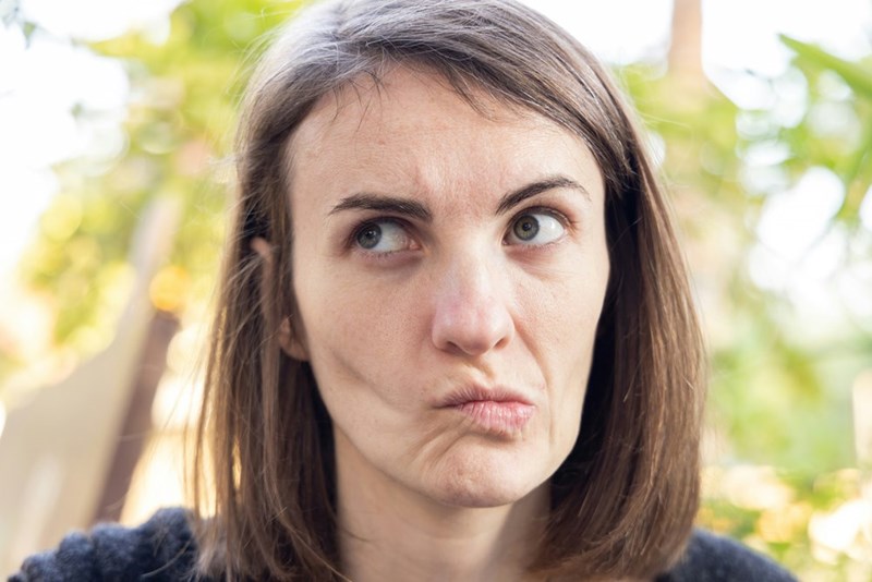 Woman looking sideways with pursed lips and a bothered expression against a blurred green background.
