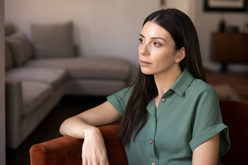 Woman in a green shirt sitting in an armchair and looking to the side in a softly lit living room.