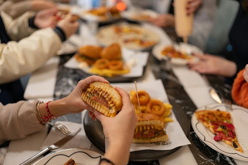 A person holds a delicious-looking sandwich while out to dinner with their family at a restaurant (models).