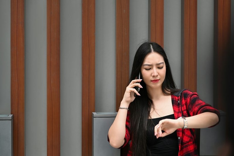 A young woman is on the phone and checking her watch, looking concerned at the time, is she late? (model)