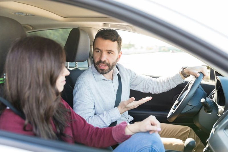 Man and woman sitting in a car with a straight face.