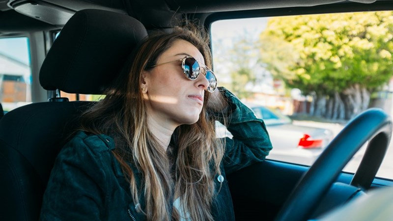 Woman wearing sunglasses sitting in the driving seat of a car.