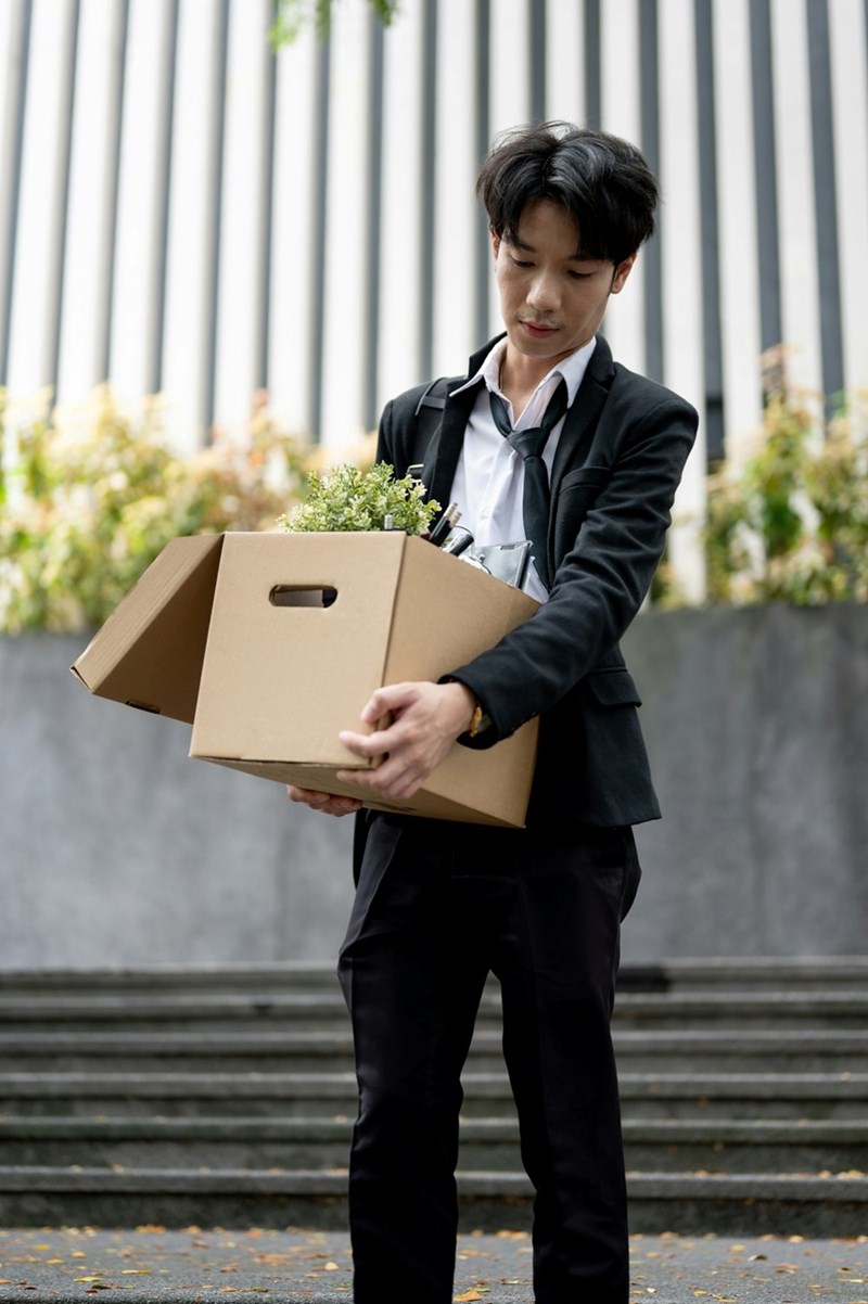 An employee carries a box of his office belongings down some stairs outside