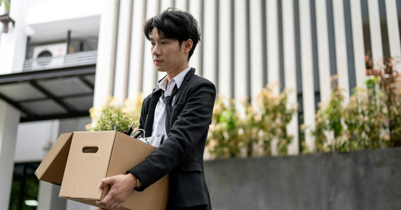 An employee looks pensive as he carries a box of his belongings outside