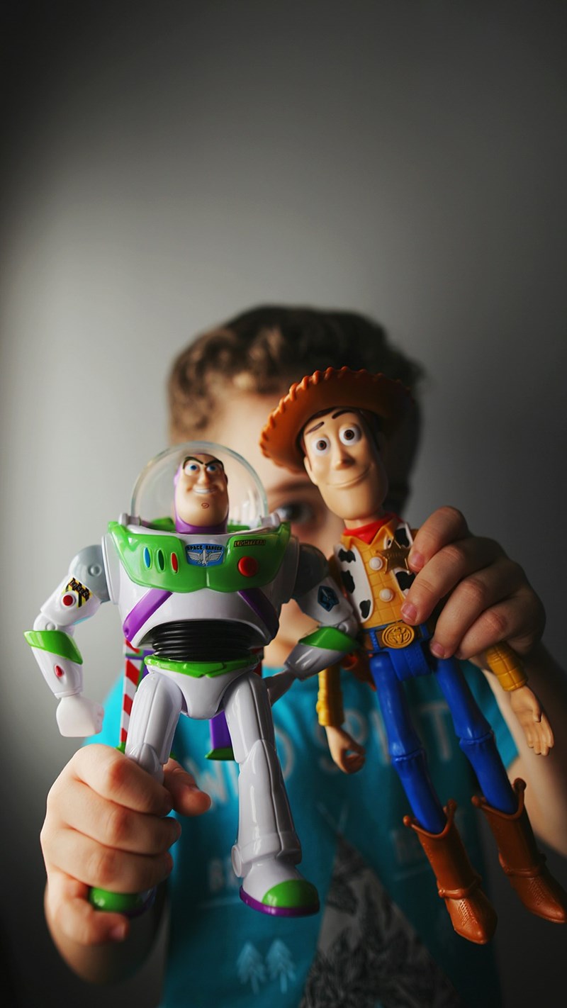 An illustration of a child holding Toy Story characters: Woody and Buzz Lightyear, playing with them during a movie premiere.