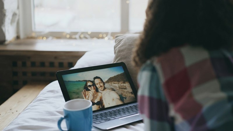 woman looks at a screen with a photo of a couple on a beach