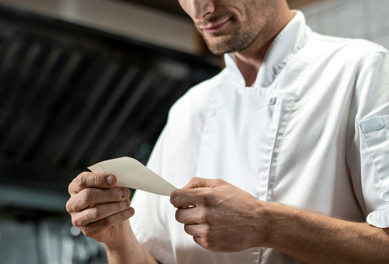 A chef reads a written note with instructions he gave, a smug look on his face.