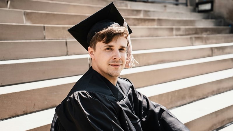 Newly graduated PhD student sitting on campus steps during graduation day.