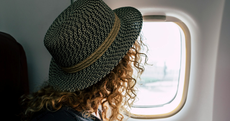 A woman wearing a hat, sitting in an airplane seat with her face turned to the window