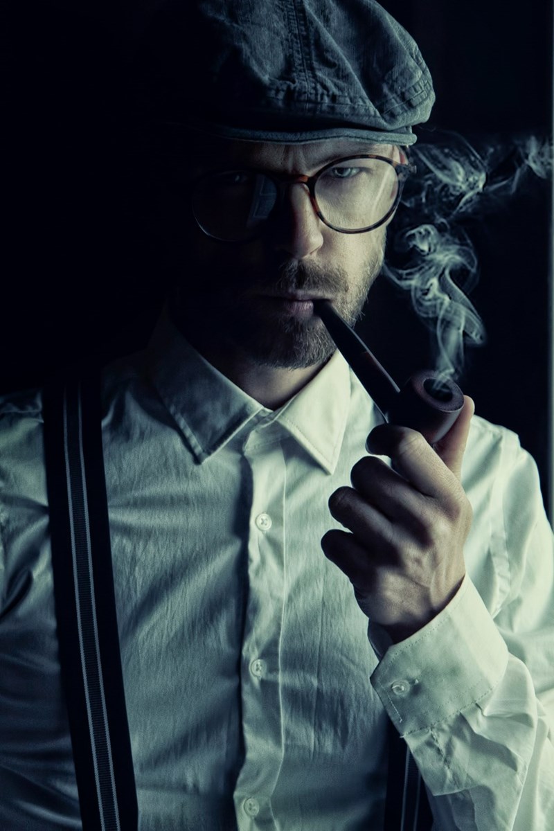 man with a hat smoking a pipe looking mysterious