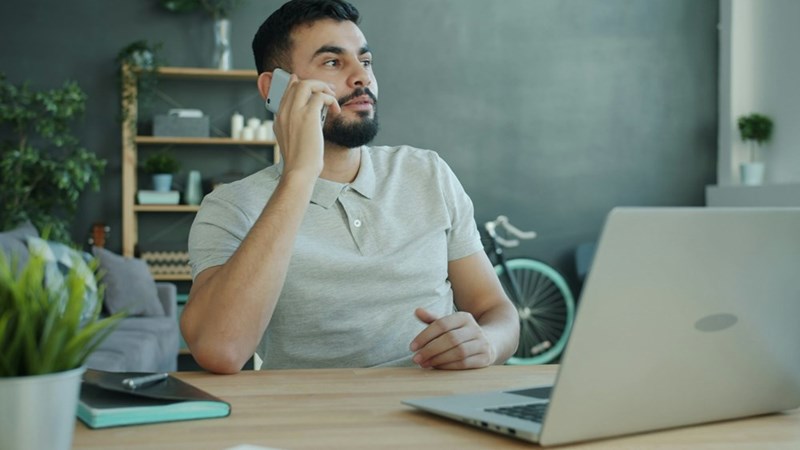employee talking on the phone while sitting at a desk with a laptop.