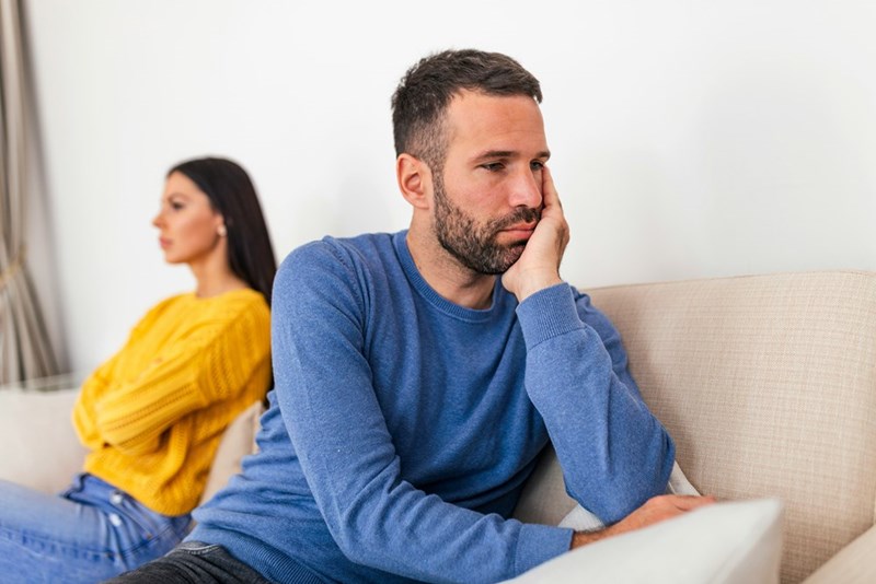 A couple sits apart on the sofa in silence