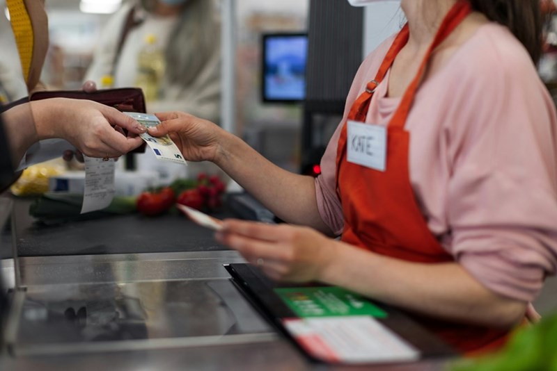 A woman hands money to a shop assistant in the supermarket