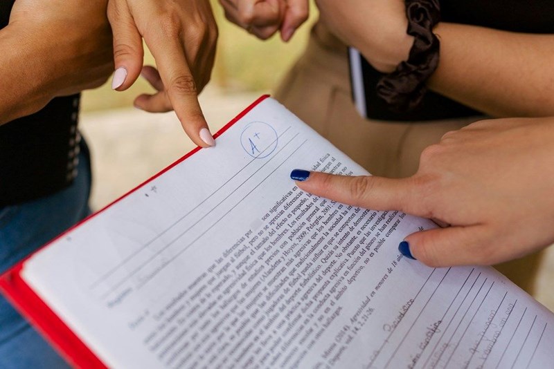 High school students gather around a grade paper and point at the A+ marking.