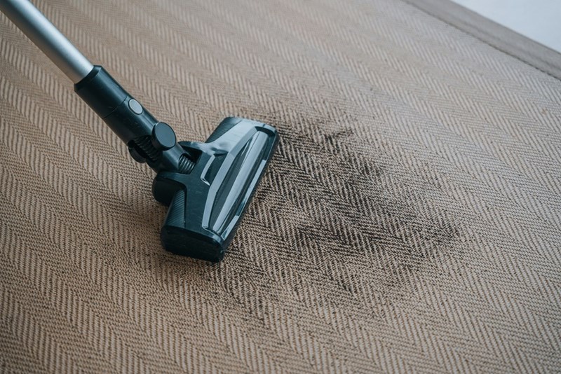 A vacuum cleaner removes dirt from a worn carpet with visible signs of everyday use.