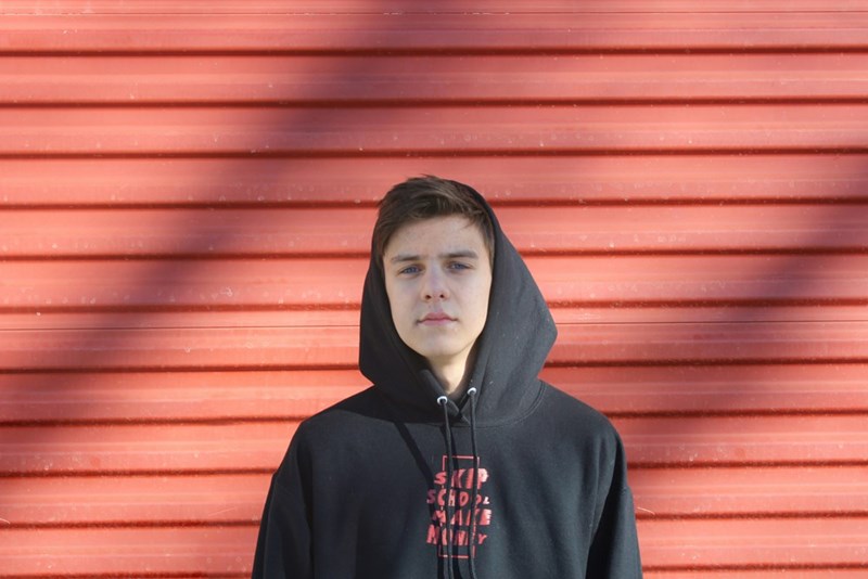 Teenage boy wearing a black hoodie stands in front of a red wall