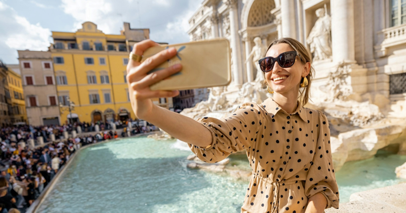 A woman takes a selfie with the Trevi Fountain behind her