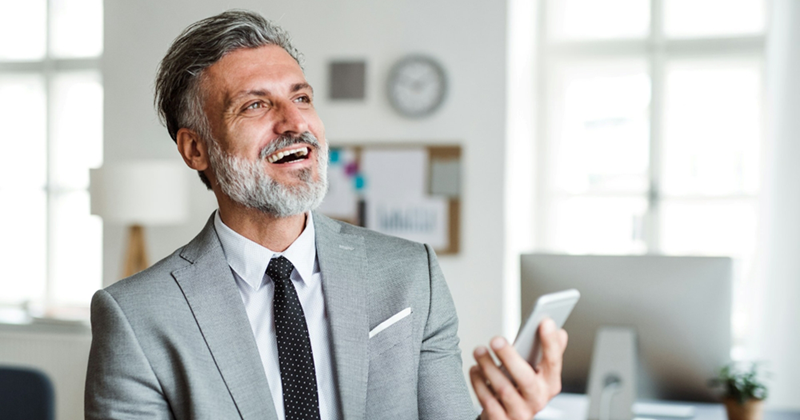 A manager wearing a suit laughs as he talks on speakerphone