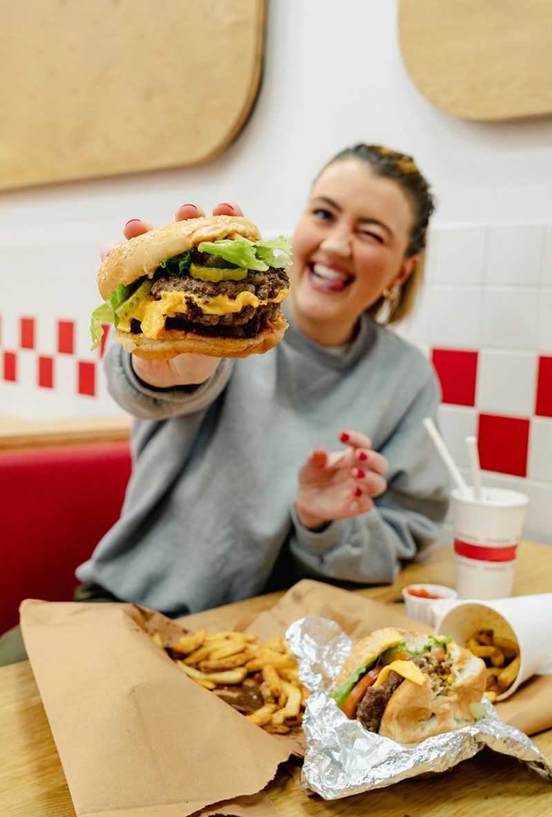 A representation of a woman who orders a burger at a casual dinner with a friend, which later becomes awkward after she packs her leftovers.