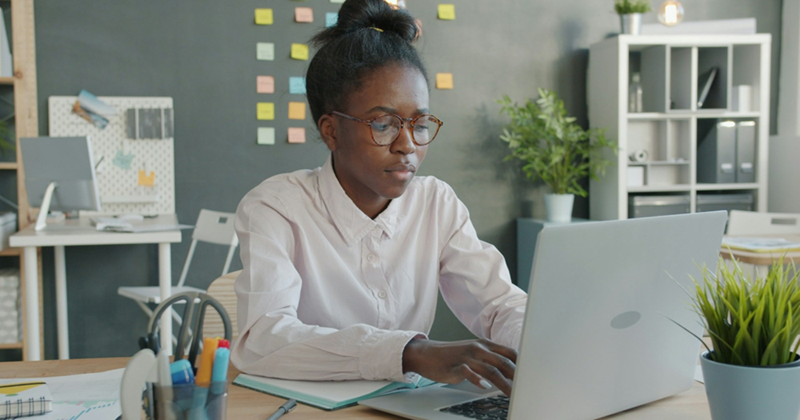 An employee sits at a desk and types something on a laptop