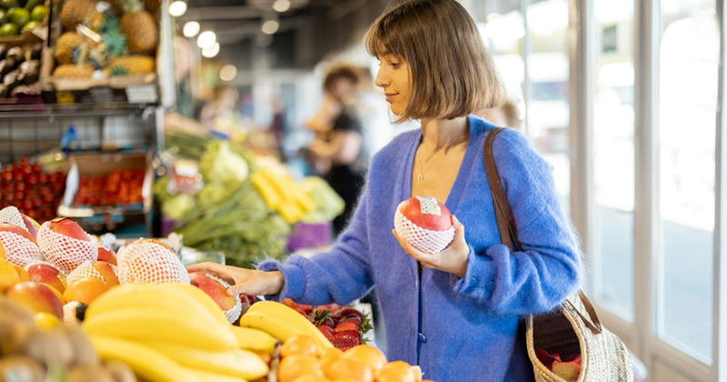 A representation of a young woman looking at mangoes in the fruit and vegetable section of a grocery store