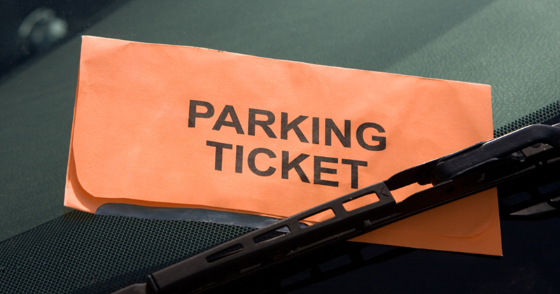 Orange parking ticket tucked under a windshield wiper on a car windshield.