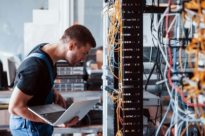 A worker works on a critical error in a server room, actor depiction.