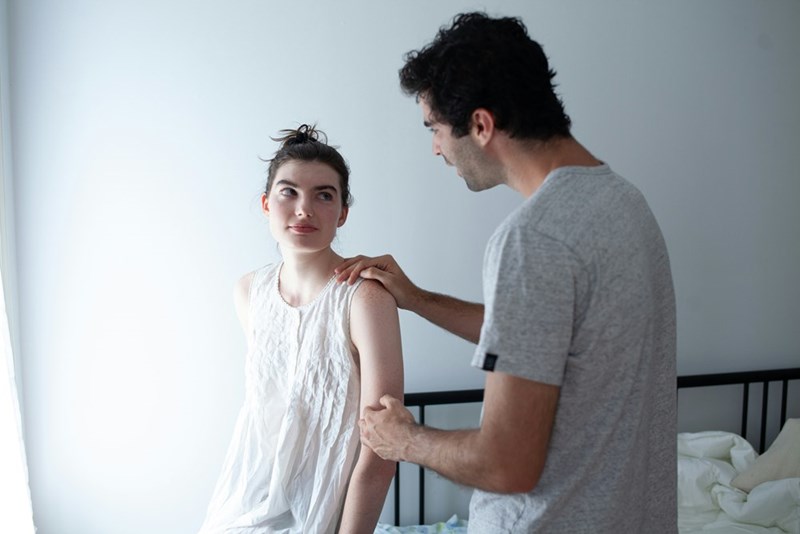 Two people stand together in a bright room, talking.