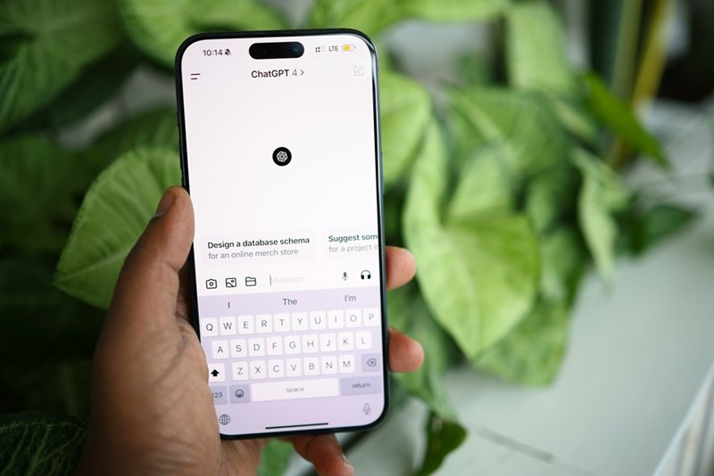 A person holds a smartphone displaying the ChatGPT app against a backdrop of green plants.